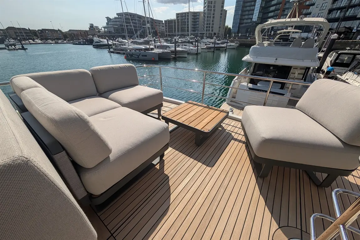 Stylish outdoor seating area on a boat deck, featuring cream cushions, a wooden table, and views of the marina.